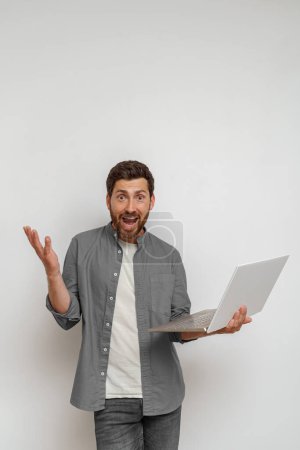 Téléchargez les photos : Homme avec ordinateur portable et écarte les mains ne sachant pas quoi faire sur fond blanc. Photo de haute qualité - en image libre de droit