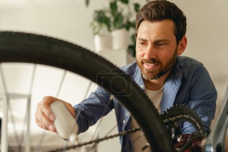 Téléchargez les photos : Gros plan de l'homme en vêtements décontractés lubrifier la chaîne de vélo avec de l'huile à la maison. Photo de haute qualité - en image libre de droit