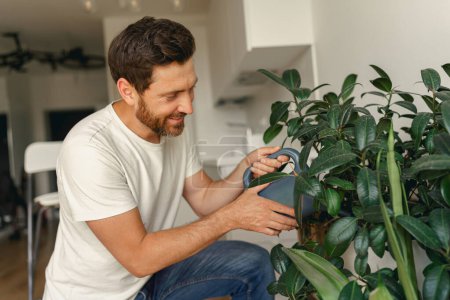 Téléchargez les photos : Homme mûr souriant arrosant des plantes à la maison. Travaux ménagers et concept de ménage. Photo de haute qualité - en image libre de droit
