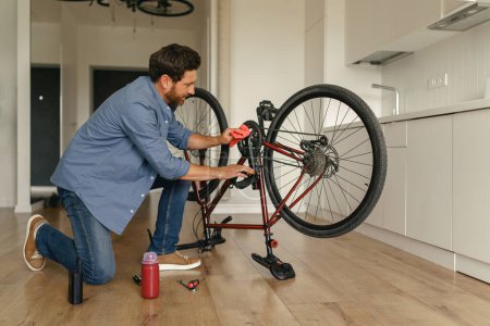 Téléchargez les photos : Beau homme en vêtements décontractés réparer le vélo lui-même à la maison. Photo de haute qualité - en image libre de droit