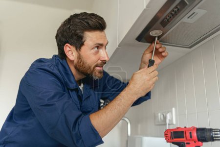 Foto de Trabajador masculino profesional en uniforme reparando campana de cocina moderna en la cocina. Foto de alta calidad - Imagen libre de derechos
