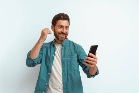 Photo for Man showing happy gesture while looking to his mobile phone on white background. High quality photo - Royalty Free Image