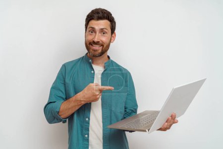 Foto de Hombre sonriente apuntando a la computadora portátil mientras está de pie sobre un fondo blanco. Foto de alta calidad - Imagen libre de derechos