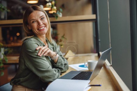 Foto de Analista mujer trabajando con documentos y utilizar el ordenador portátil mientras está sentado en coworking cerca de la ventana - Imagen libre de derechos