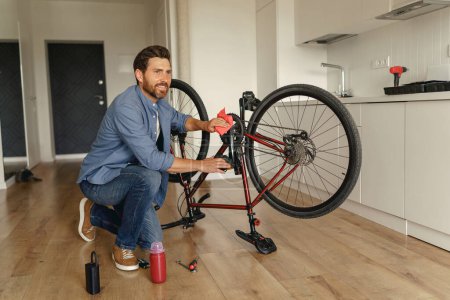 Téléchargez les photos : Beau homme en vêtements décontractés réparer le vélo lui-même à la maison. Photo de haute qualité - en image libre de droit