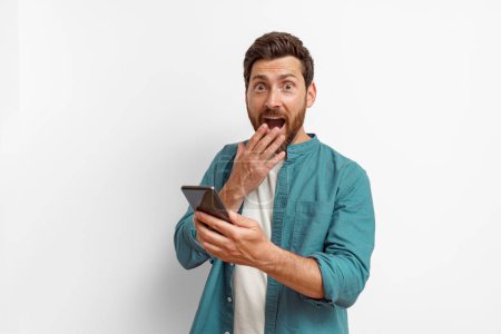 Photo for Surprised man holding mobile phone while standing on white background. High quality photo - Royalty Free Image