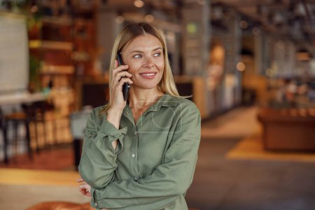 Foto de Primer plano de la mujer de negocios sonriente está hablando por teléfono con el cliente mientras está de pie en la cafetería - Imagen libre de derechos