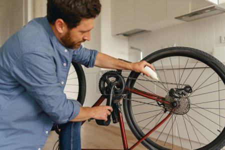 Photo for Close up of man in casual clothing lubricate the bike chain with oil at home. High quality photo - Royalty Free Image