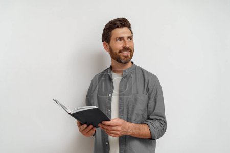 Téléchargez les photos : Homme freelance debout avec bloc-notes ouvert et regardant côté sur fond blanc - en image libre de droit