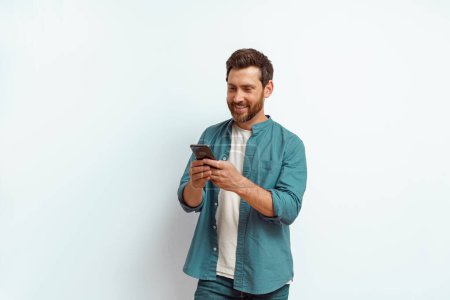 Téléchargez les photos : Homme regardant son téléphone portable tout en se tenant debout sur fond blanc. Photo de haute qualité - en image libre de droit