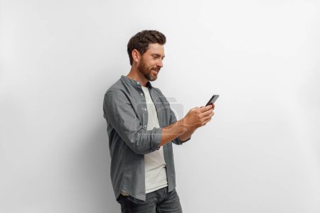 Photo for Man looking to his mobile phone while standing on white background. High quality photo - Royalty Free Image