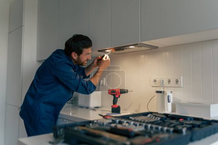 Foto de Trabajador masculino profesional en uniforme reparando campana de cocina moderna en la cocina. Foto de alta calidad - Imagen libre de derechos