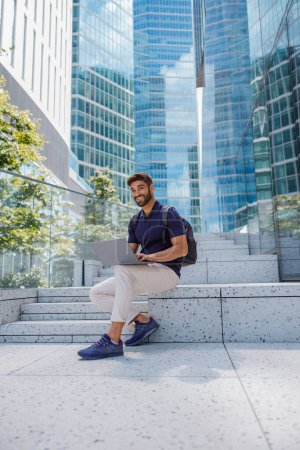 Téléchargez les photos : Homme d'affaires assis avec ordinateur portable sur fond de gratte-ciel de la ville. Photo de haute qualité - en image libre de droit