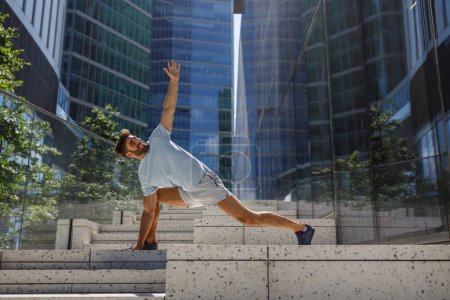 Photo for Healthy sporty man doing stretch on modern city skyscrapers background. High quality photo - Royalty Free Image