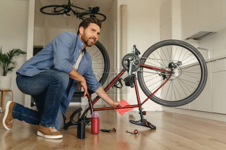 Téléchargez les photos : Beau homme en vêtements décontractés nettoie le vélo de la saleté après réparation à la maison. Photo de haute qualité - en image libre de droit
