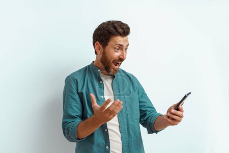 Photo for Man showing happy gesture while looking to his mobile phone on white background. High quality photo - Royalty Free Image