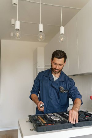Téléchargez les photos : Travailleur masculin avec boîte à outils debout sur fond de cuisine maison. Photo de haute qualité - en image libre de droit