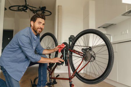 Photo for Handsome man in casual clothing cleans the bike from dirt after repair at home. High quality photo - Royalty Free Image