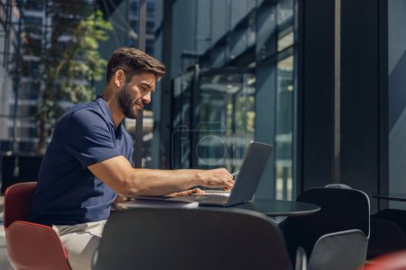Téléchargez les photos : Homme d'affaires concentré travaillant sur ordinateur portable assis dans le bureau pendant la journée de travail - en image libre de droit