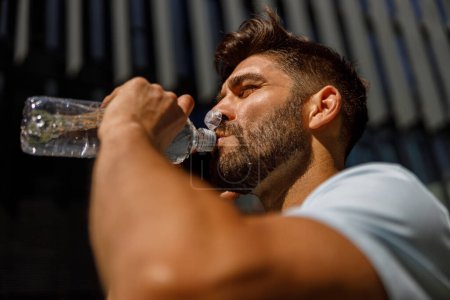 Photo for Close up of sport man drinking water after running in the city skyscrapers background - Royalty Free Image