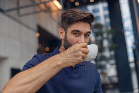 Foto de Primer plano de hombre barbudo guapo bebiendo café en el fondo de coworking moderno. Foto de alta calidad - Imagen libre de derechos
