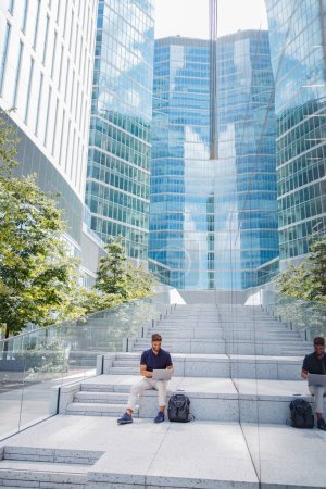 Photo for Businessman sitting with laptop on city skyscrapers background. High quality photo - Royalty Free Image