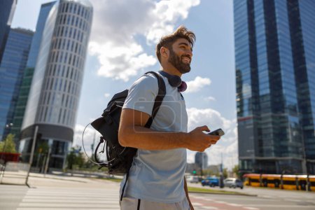 Photo for Man with phone standing on skyscrapers background after training and looks away - Royalty Free Image