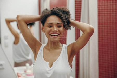 Photo for Smiling young woman showing smooth armpits standing in bathroom. Hair removal concept - Royalty Free Image
