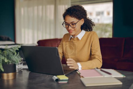 Téléchargez les photos : Attrayant femme d'affaires travaillant à distance sur ordinateur portable de la maison tout en étant assis au salon - en image libre de droit