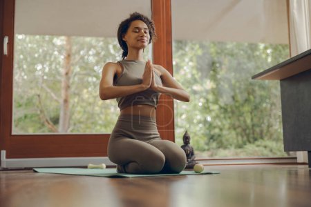 Foto de Hermosa mujer fitness meditar mientras hace yoga en el interior en casa en la estera - Imagen libre de derechos