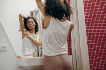 Téléchargez les photos : Jeune femme souriante se rasant les aisselles avec un rasoir dans la salle de bain à la maison. Épilation domestique - en image libre de droit