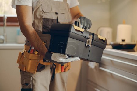 Téléchargez les photos : Gros plan du réparateur en uniforme debout sur la cuisine de la maison et tenant son sac à outils - en image libre de droit