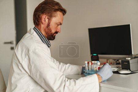 Téléchargez les photos : Un homme en uniforme scientifique tient des éprouvettes en laboratoire. - en image libre de droit