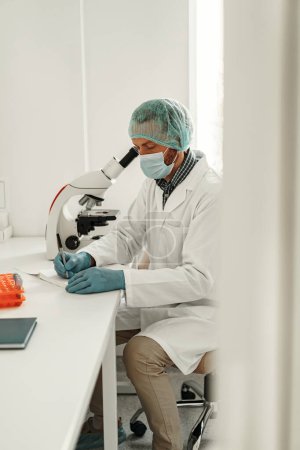 Foto de Científico masculino haciendo notas en un bloc de notas mientras hace pruebas dentro de un laboratorio de investigación - Imagen libre de derechos