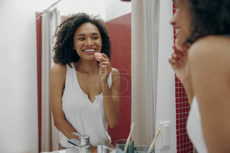 Téléchargez les photos : Femme regardant dans le miroir dans la salle de bain tout en démaquillant ou en faisant la routine de nettoyage - en image libre de droit