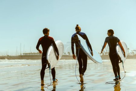 Foto de Grupo de amigos con tablas de surf entrando hacia el océano para surfear sobre las olas. Foto de alta calidad - Imagen libre de derechos