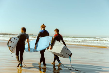 Foto de Grupo de amigos con tablas de surf entrando hacia el océano para surfear sobre las olas. Foto de alta calidad - Imagen libre de derechos