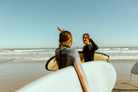 Foto de Surfer se encuentra con un amigo saludando con la mano mientras lleva la tabla de surf en la playa. Foto de alta calidad - Imagen libre de derechos