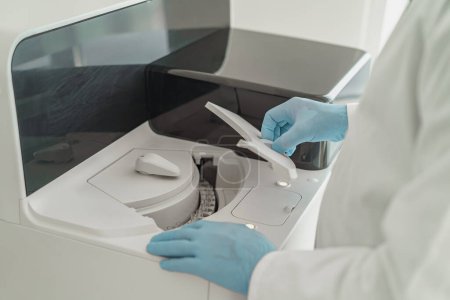 Téléchargez les photos : Gros plan de la main du chercheur dans un gant stérile mettant un tube en plastique dans une centrifugeuse de laboratoire - en image libre de droit
