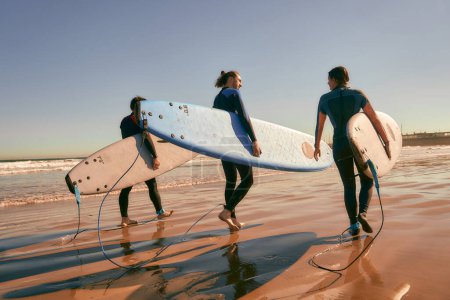 Foto de Grupo de surfistas con tablas de surf en traje de neopreno están caminando en la playa después de montar las olas - Imagen libre de derechos