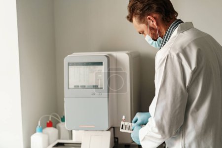 Foto de Hombre vistiendo uniforme científico y máscara está sosteniendo tubos de ensayo en el laboratorio - Imagen libre de derechos