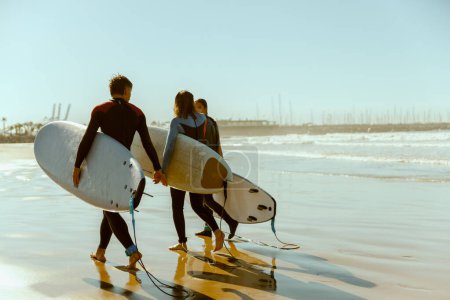 Foto de Surfistas felices en traje de neopreno con sus tablas de surf entrando fuera del mar después de surfear en las olas - Imagen libre de derechos