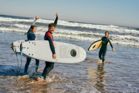 Téléchargez les photos : Les surfeurs rencontrent des amis en agitant la main tout en portant une planche de surf sur la plage. Photo de haute qualité - en image libre de droit