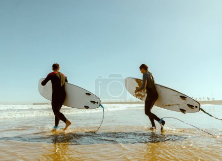 Photo for Group of friends with surfboards entering towards ocean for surfing on waves. High quality photo - Royalty Free Image