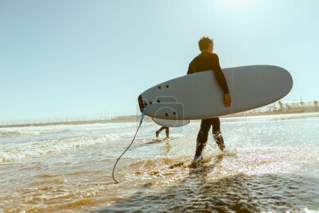 Foto de Hombre surfista en traje de neopreno con su tabla de surf entrando en el mar. Surfeando en el océano. Foto de alta calidad - Imagen libre de derechos