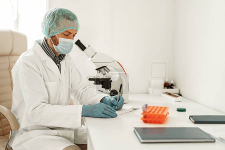 Foto de Científico masculino haciendo notas en un bloc de notas mientras hace pruebas dentro de un laboratorio de investigación - Imagen libre de derechos