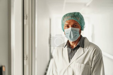 Photo for Professional doctor in uniform and mask standing at hospital and looking at camera - Royalty Free Image