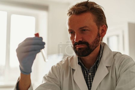 Photo for Man wearing scientist uniform and mask is holding test tube at laboratory - Royalty Free Image
