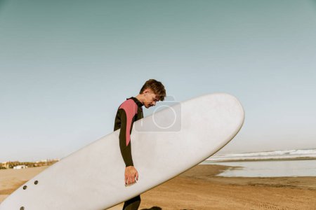 Foto de Hombre surfista en traje de neopreno con su tabla de surf entrando en el mar. Surf y océano. Foto de alta calidad - Imagen libre de derechos