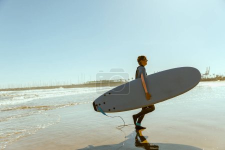 Foto de Surfista femenina en traje de neopreno con su tabla de surf entrando fuera del mar después de surfear en las olas - Imagen libre de derechos